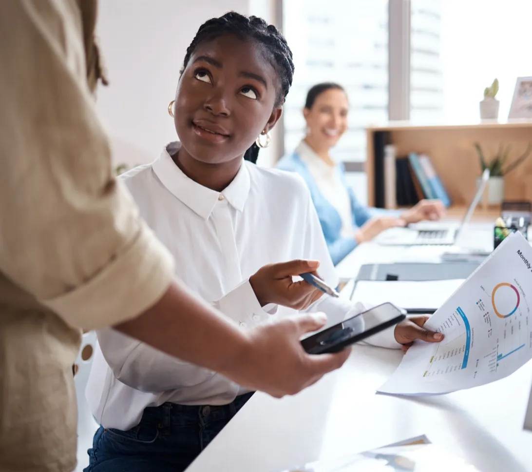 A recruitment consultant talking through paperwork with a colleague at her desk